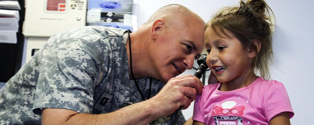 Army doctor examining little girl's ears
